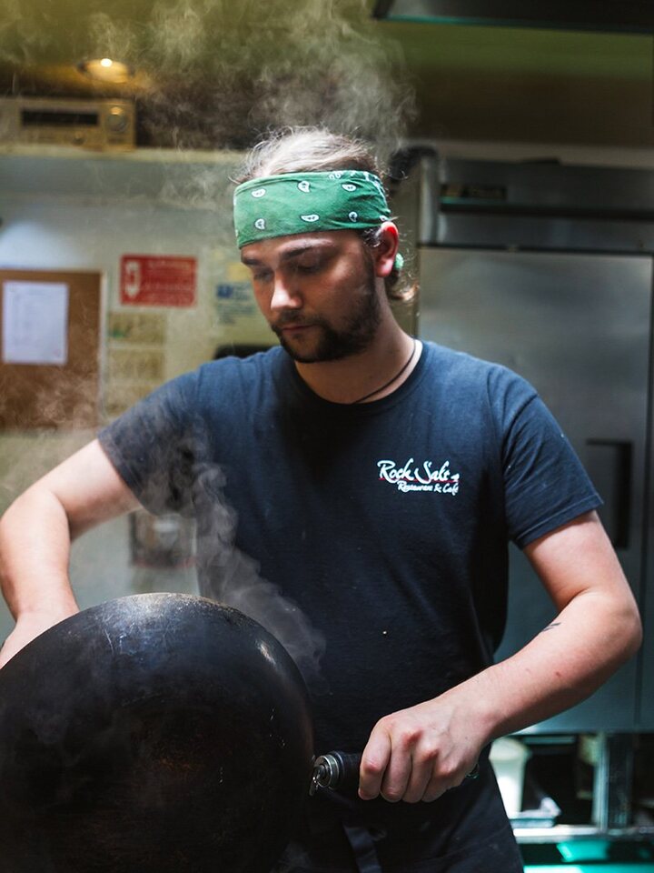 A Rock Salt cook working a steaming wok in the kitchen